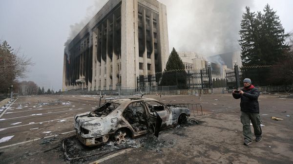 Мужчина фотографирует сгоревший автомобиль перед зданием мэрии Алматы (6 января 2022). Казахстан - Sputnik Армения
