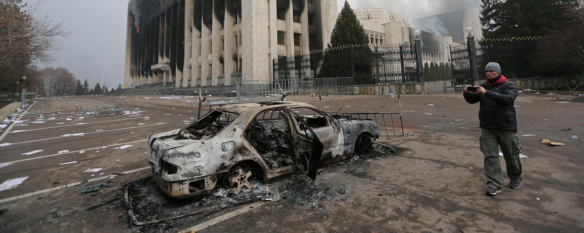 Мужчина фотографирует сгоревший автомобиль перед зданием мэрии Алматы (6 января 2022). Казахстан - Sputnik Армения, 1920, 07.01.2022