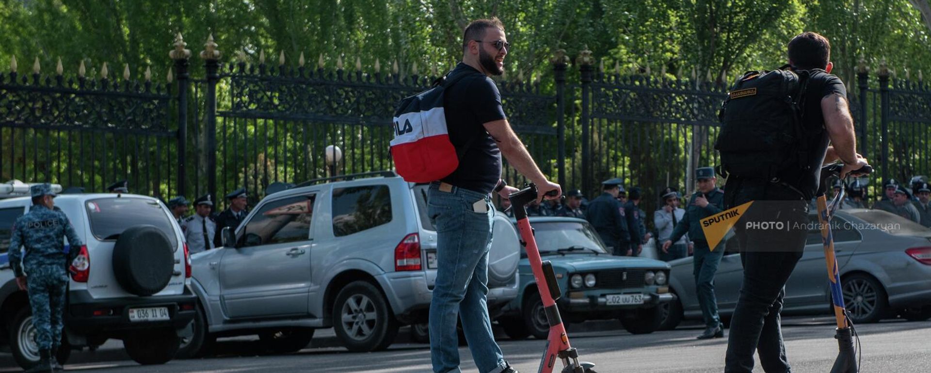 Молодые люди проезжают на электросамокатах мимо полицейского кордона у здания Парламента (4 мая 2022). Еревaн - Sputnik Армения, 1920, 29.06.2022