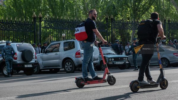 Молодые люди проезжают на электросамокатах мимо полицейского кордона у здания Парламента (4 мая 2022). Еревaн - Sputnik Армения