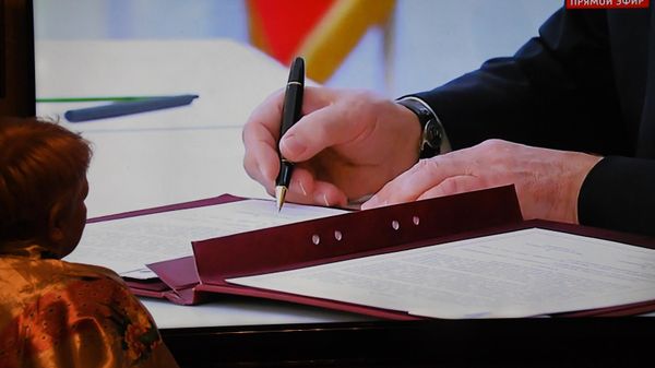 Женщина смотрит на экране, как Владимир Путин подписывает договоры о вхождении в Российскую Федерацию Донецкой и Луганской народных республик, Запорожской и Херсонской областей (30 сентября 2022). Москва - Sputnik Армения