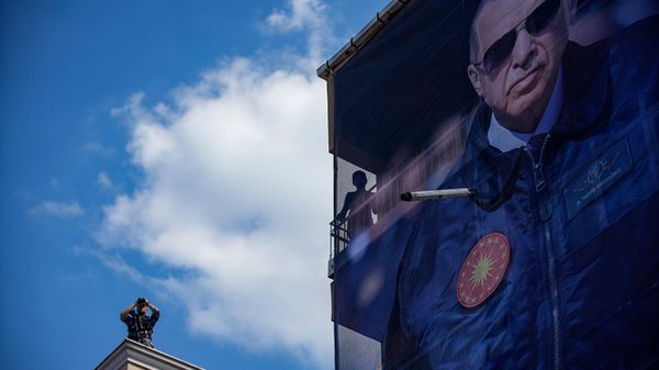 Полицейский с биноклем на крыше здания рядом с гигантским баннером с изображением президента Турции Реджепа Тайипа Эрдогана во время предвыборного митинга (13 мая 2023). Стамбул - Sputnik Армения
